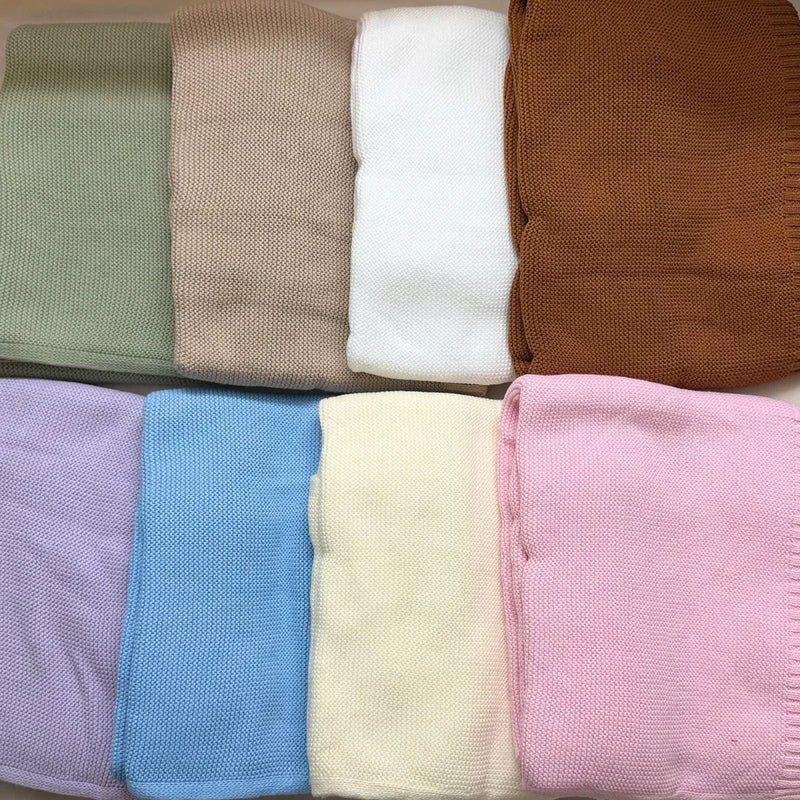 Eight knit cotton baby blankets laid flat, one in each color