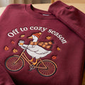Off to Cozy Season Goose Riding Bicycle Fall Leaves Coffee embroidered sweatshirt — front view