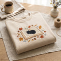 Black Cat Sleeping Open Book Autumn Leaves Acorns Mushrooms Floral embroidered sweatshirt — front view