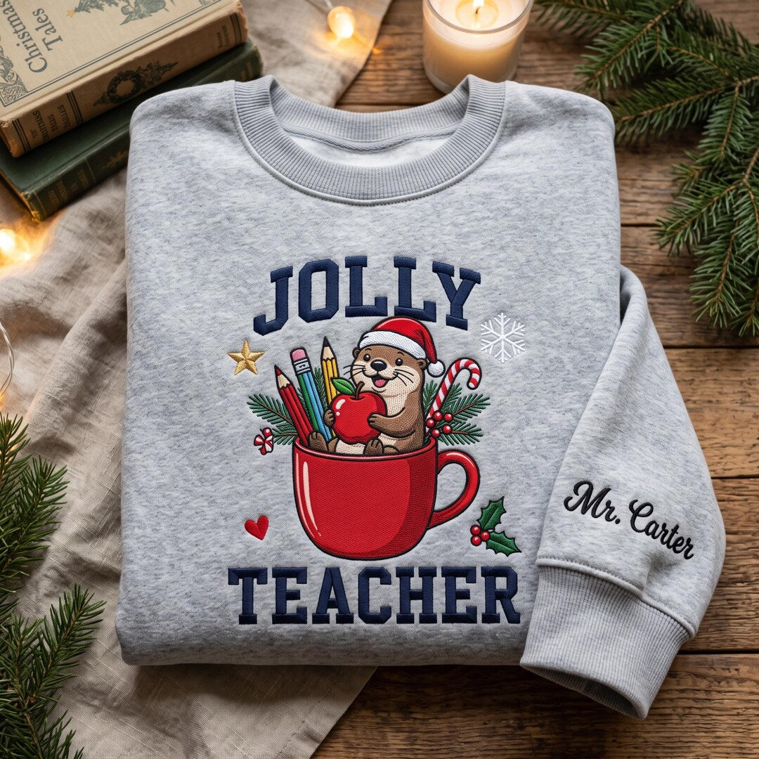 Personalized Jolly Teacher Otter Santa Hat Mug Christmas Pencils Apple embroidered sweatshirt — front view