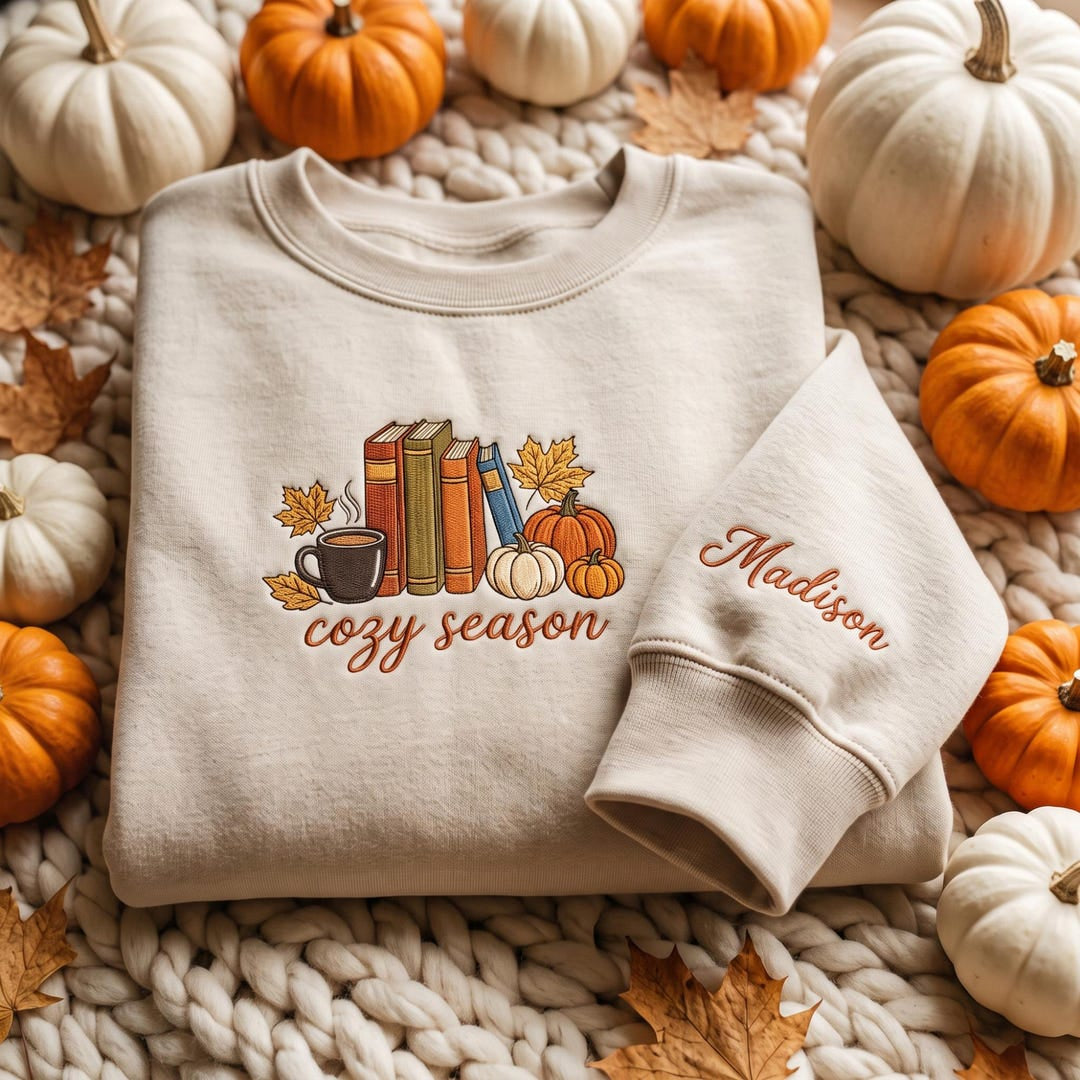 Personalized Cozy Season Stacked Books Coffee Cup Pumpkins Maple Leaves Fall Sleeve Name embroidered sweatshirt — front view