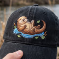 Otter Reading Book Floating River Cattails Leaves Embroidered Hat — Washed Hat